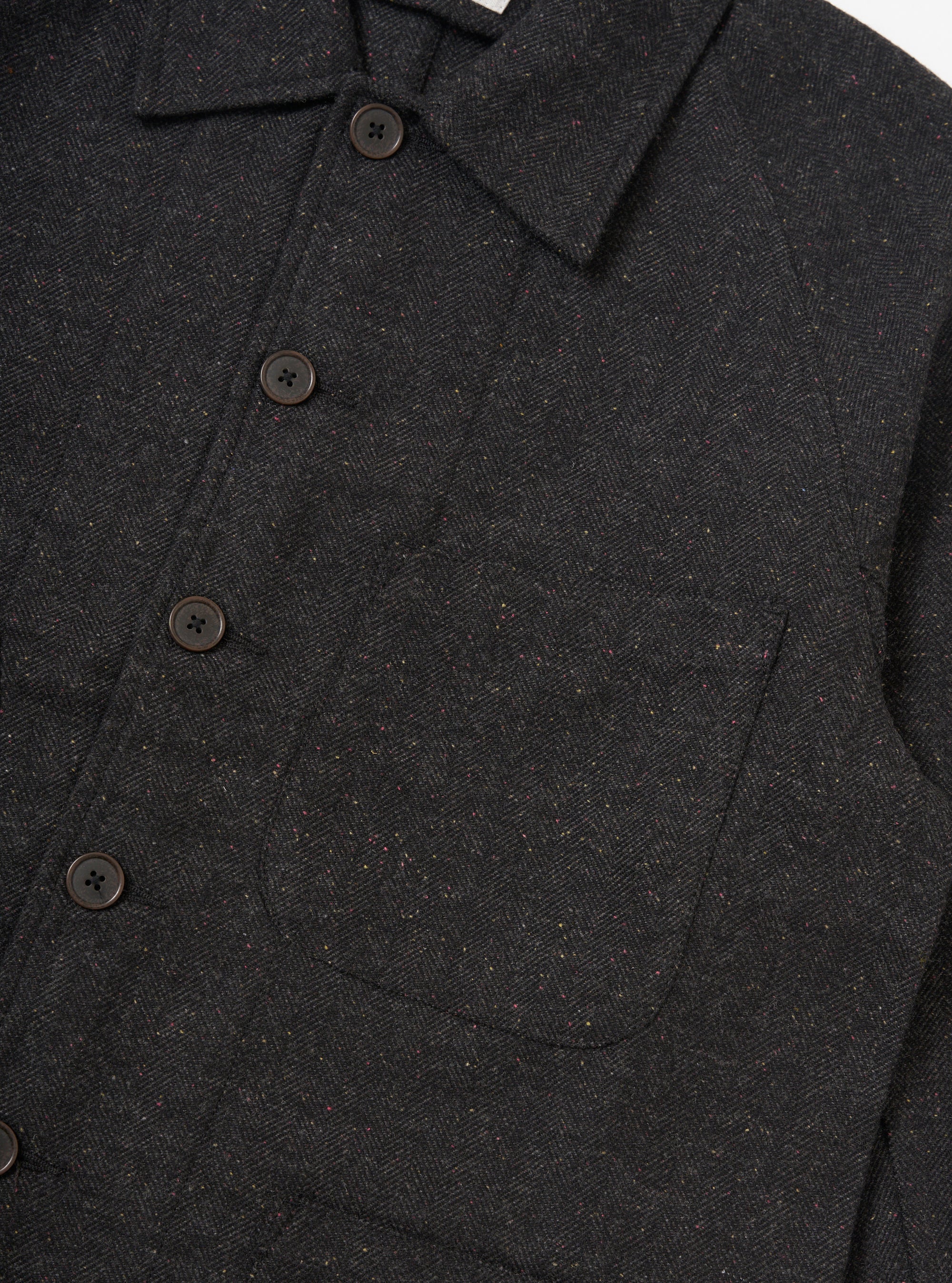 Close-up of the Black Salt N Pepper Tweed Station Jacket. The tweed is dark with flecks of color. Features brown buttons and a pocket. Shot on a white background.