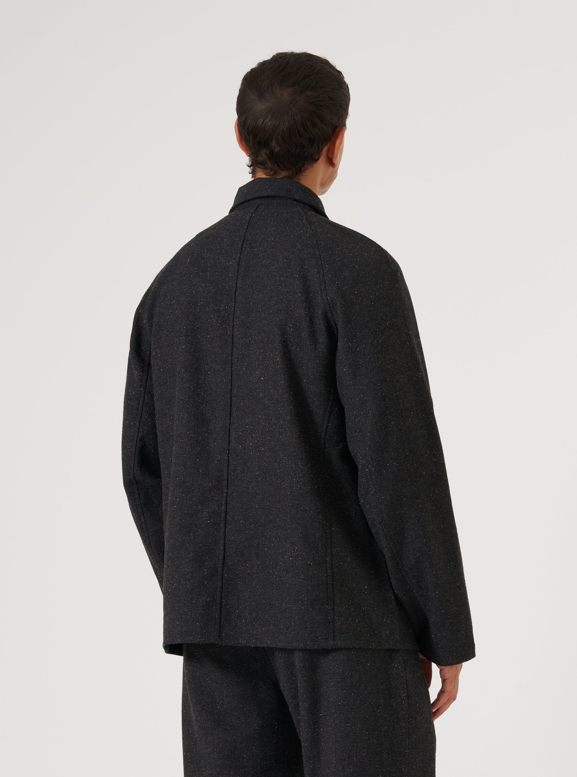 Back view of a model wearing a Black Salt N Pepper Tweed Station Jacket. The jacket is tweed and the background is a clean white.