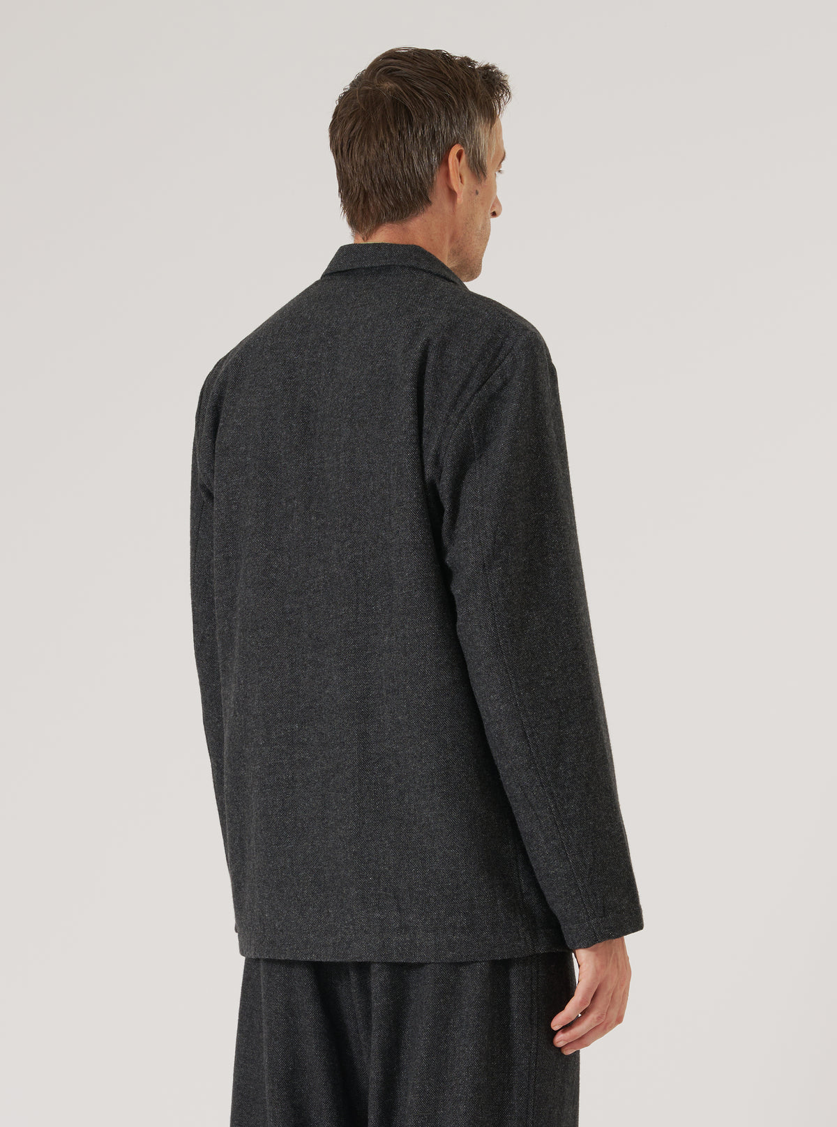 Back view of a model wearing the Grey Anders Wool Upcycled Two Button Jacket. The jacket is grey wool and has a two-button closure. Shot against a plain white backdrop.
