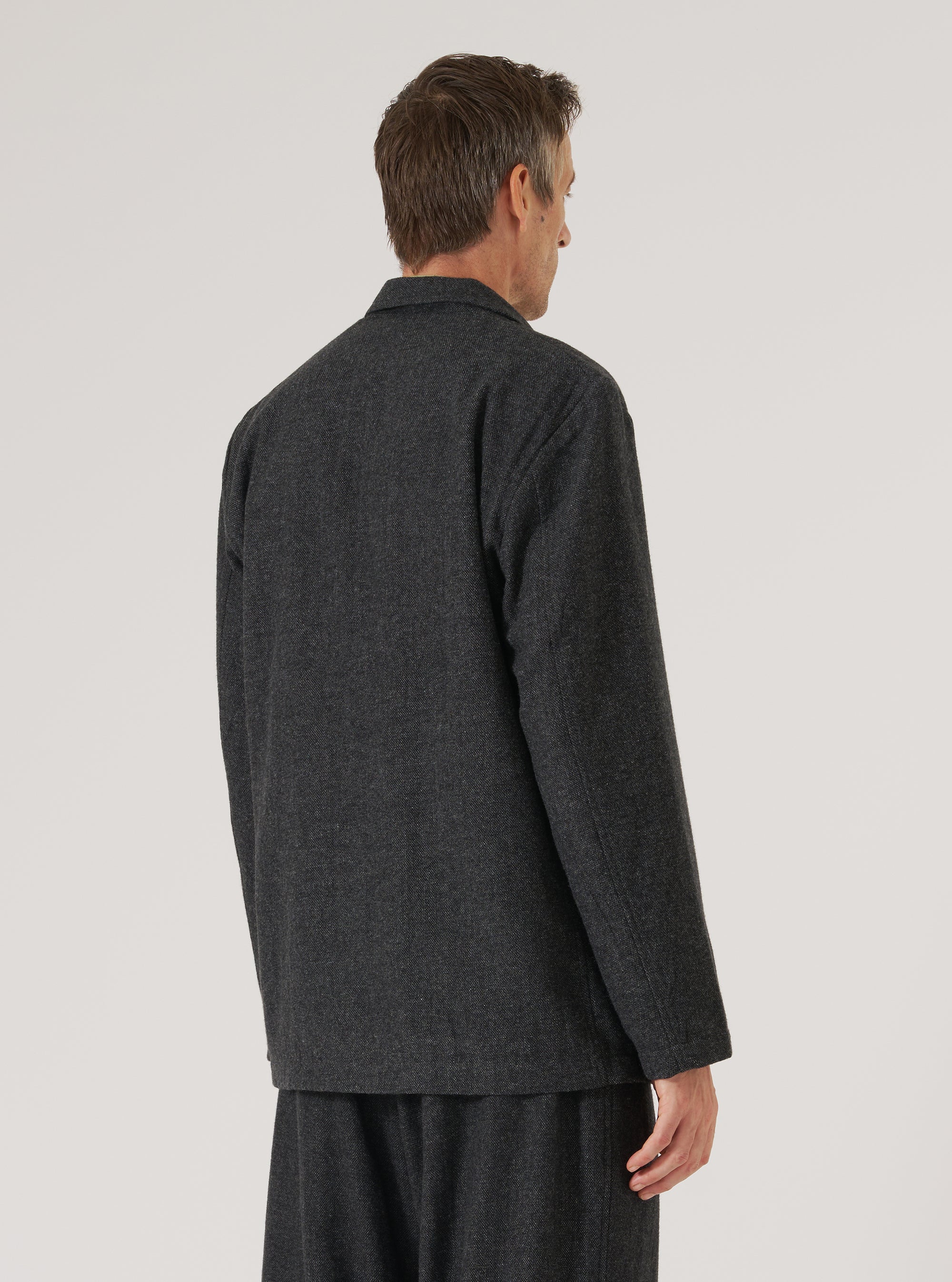 Back view of a model wearing the Grey Anders Wool Upcycled Two Button Jacket. The jacket is grey wool and has a two-button closure. Shot against a plain white backdrop.