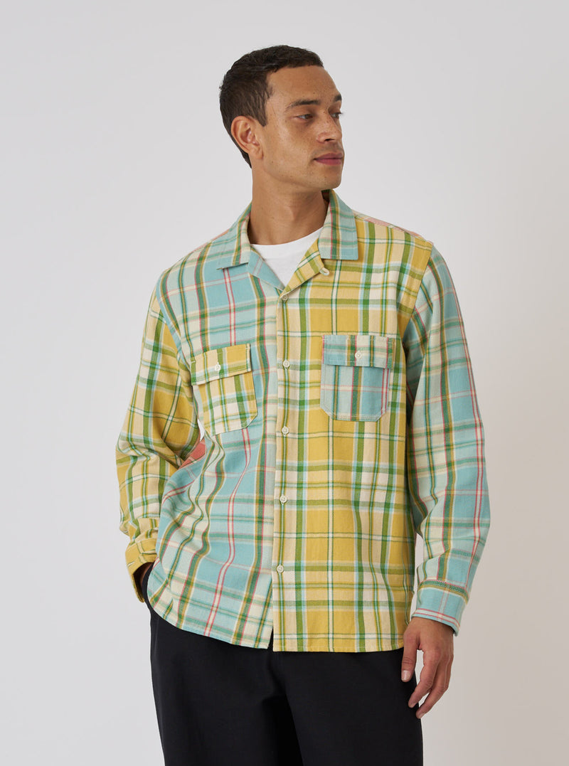 A model poses in front of a white background wearing a Faded Mixed Check Panel Shirt. The shirt is a mix of yellow and blue plaid with two chest pockets.