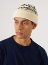 A model wears the Ecru/Navy British Wool Short Watch Cap against a white backdrop. The cap features a patterned design in ecru, navy, and gold.