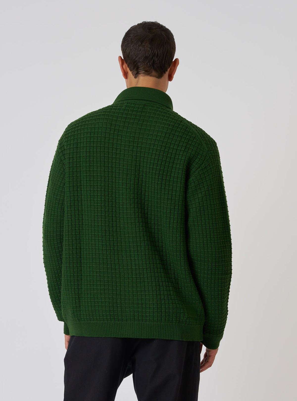 Back view of a model wearing a green textured merino knit Charlie Cardigan. The cardigan has a unique knit pattern. Shot against a plain white background.