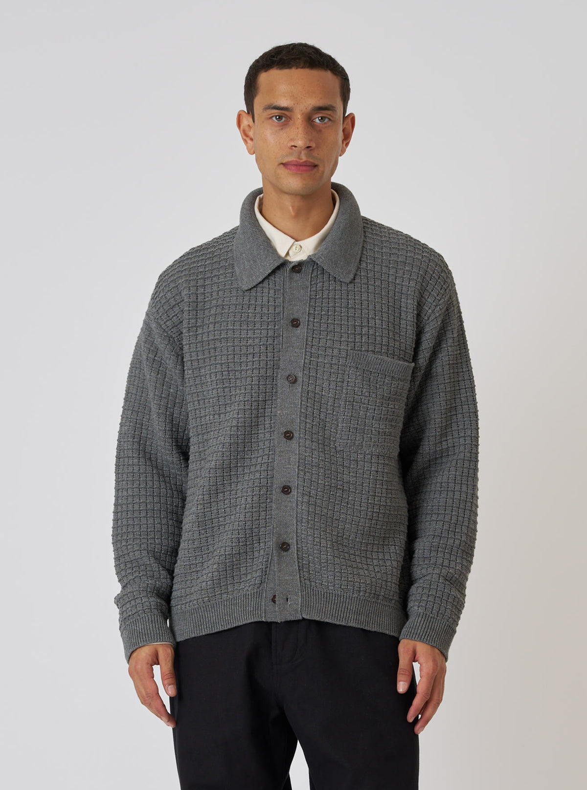 A model wears a Grey Textured Merino Knit Charlie Cardigan, buttoned up, against a white background. The cardigan has a collared neck and a pocket.