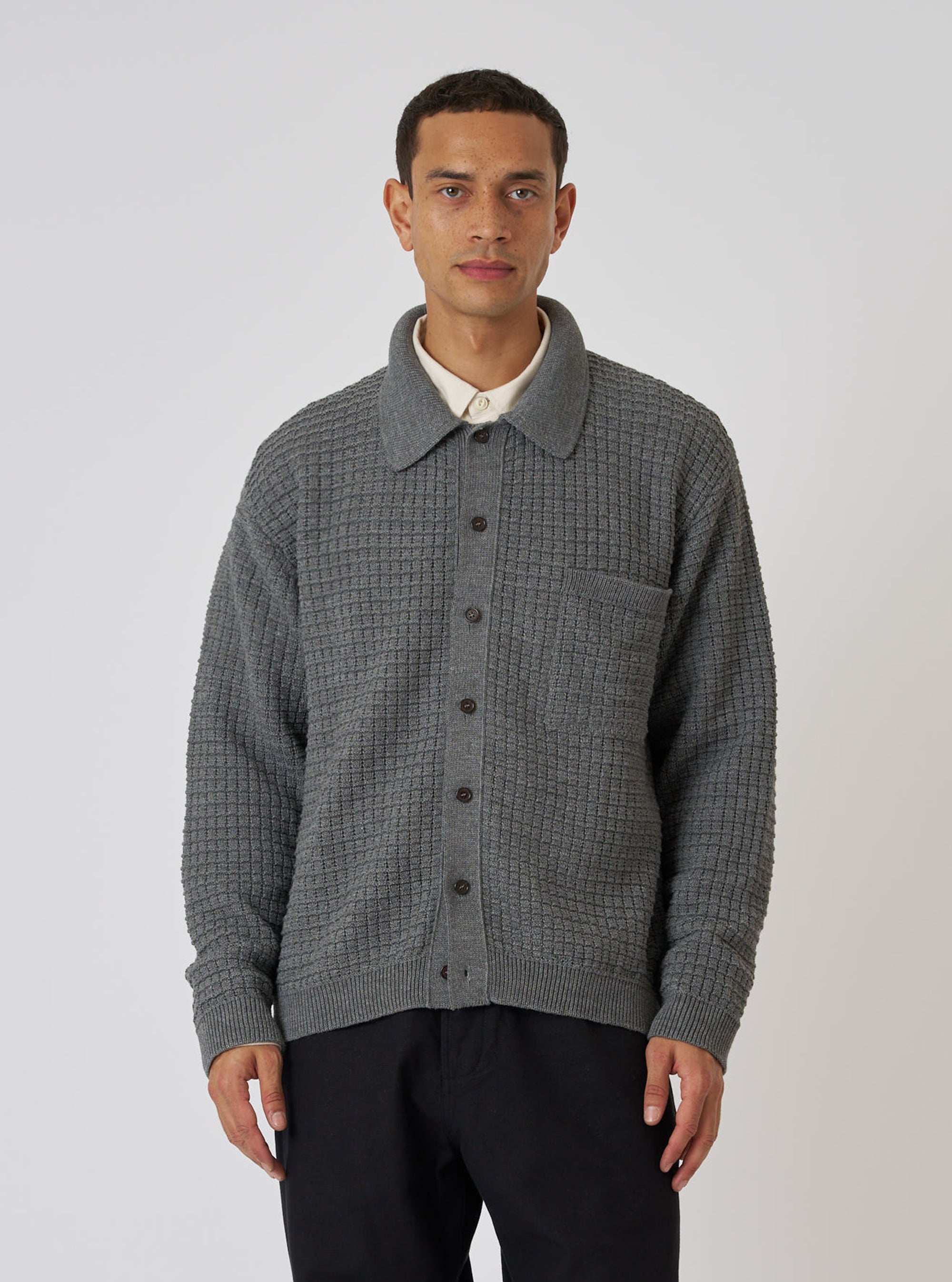 A model wears a Grey Textured Merino Knit Charlie Cardigan, buttoned up, against a white background. The cardigan has a collared neck and a pocket.