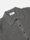 Close-up of the grey textured Merino knit Charlie Cardigan on a white background. The cardigan has a collared neck and brown buttons.