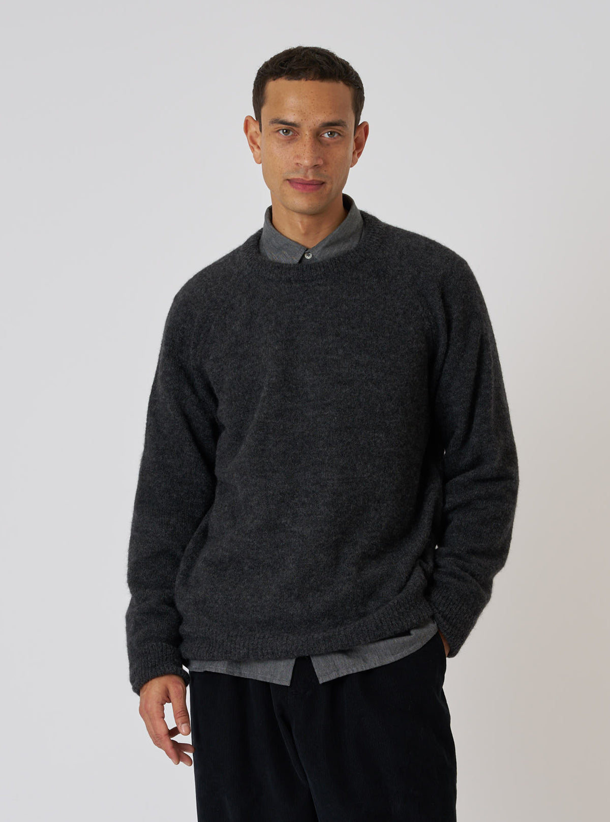 A model poses in a Charcoal Alpaca Knit Lyon Crew sweater. The relaxed-fit sweater is paired with a gray shirt and black pants against a plain white backdrop.