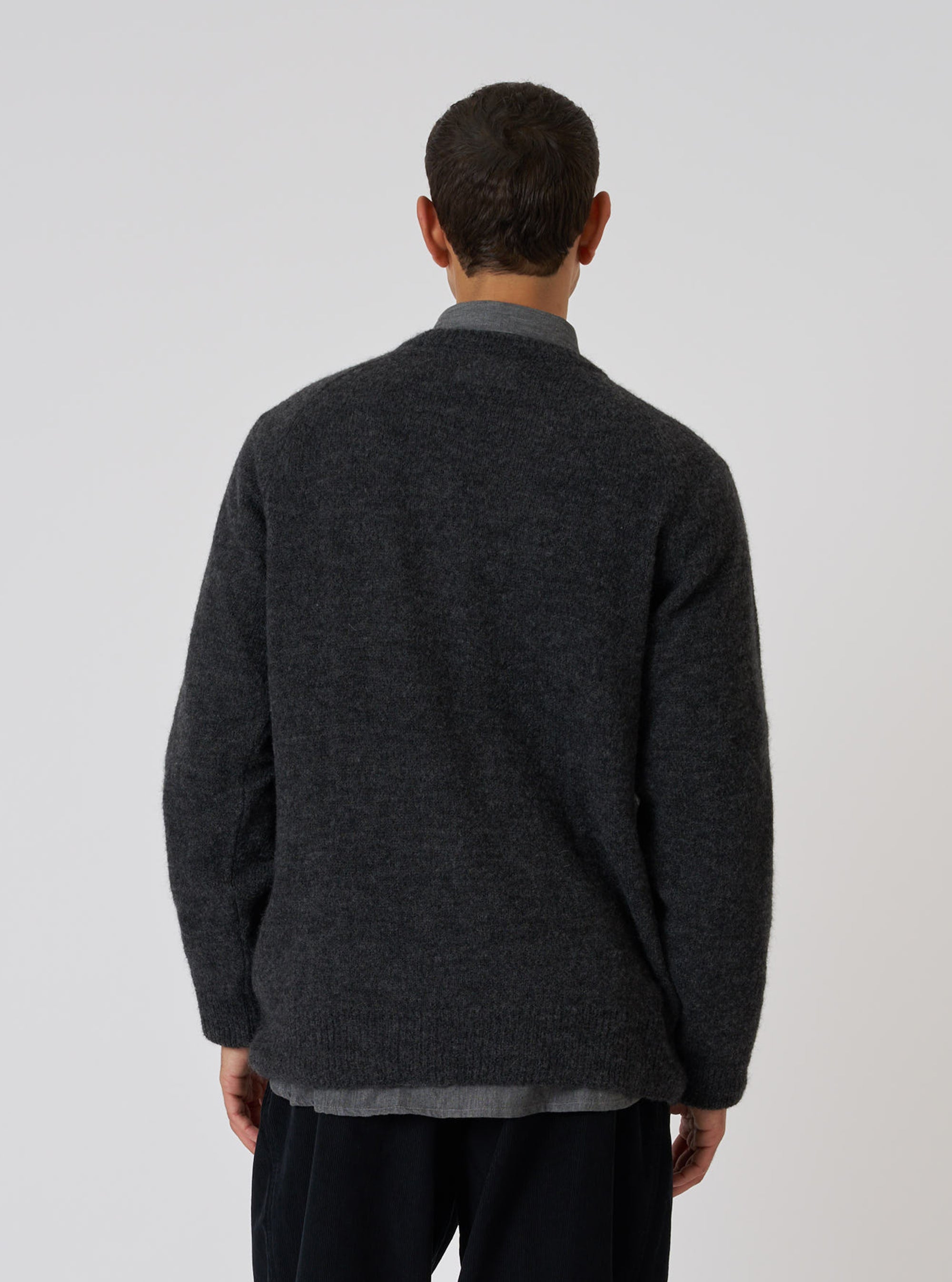 Back view of a model wearing a Charcoal Alpaca Knit Lyon Crew sweater in a studio setting. The sweater has a relaxed fit. The background is a plain white backdrop.