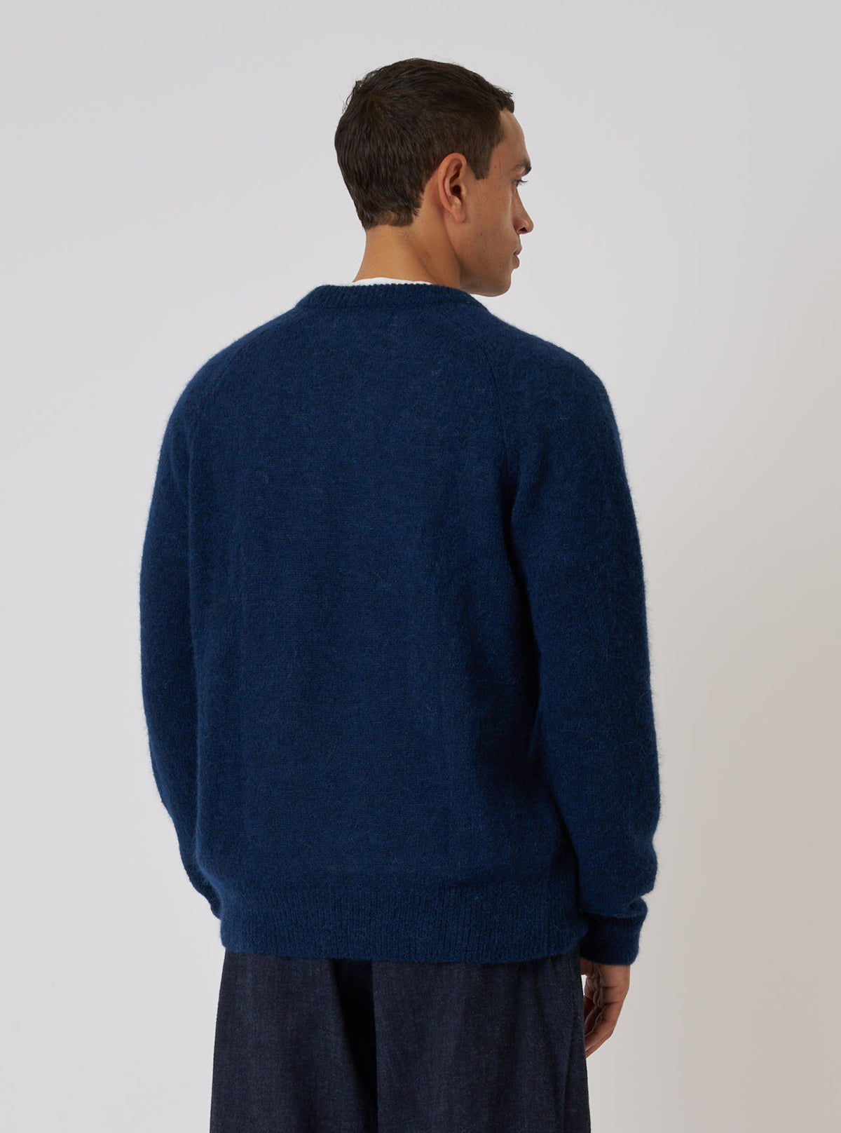 Model from behind wears a Navy Alpaca Knit Lyon Crew sweater. The soft, textured sweater is paired with dark pants against a plain white backdrop.