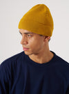 A man models the Gold Merino Knit Watch Cap against a white backdrop. The gold knit cap is paired with a navy tee.
