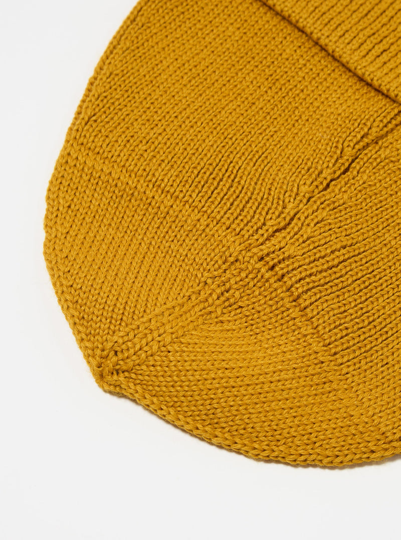 Close-up of a gold Merino Knit Watch Cap on a white surface. The knit texture is visible, showcasing the quality of the merino wool.