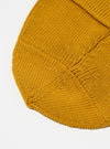 Close-up of a gold Merino Knit Watch Cap on a white surface. The knit texture is visible, showcasing the quality of the merino wool.