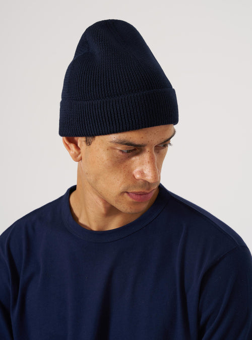A man models the Navy Merino Knit Watch Cap against a plain white background. The close-up shot highlights the cap's knit texture and fit, paired with a matching navy t-shirt.