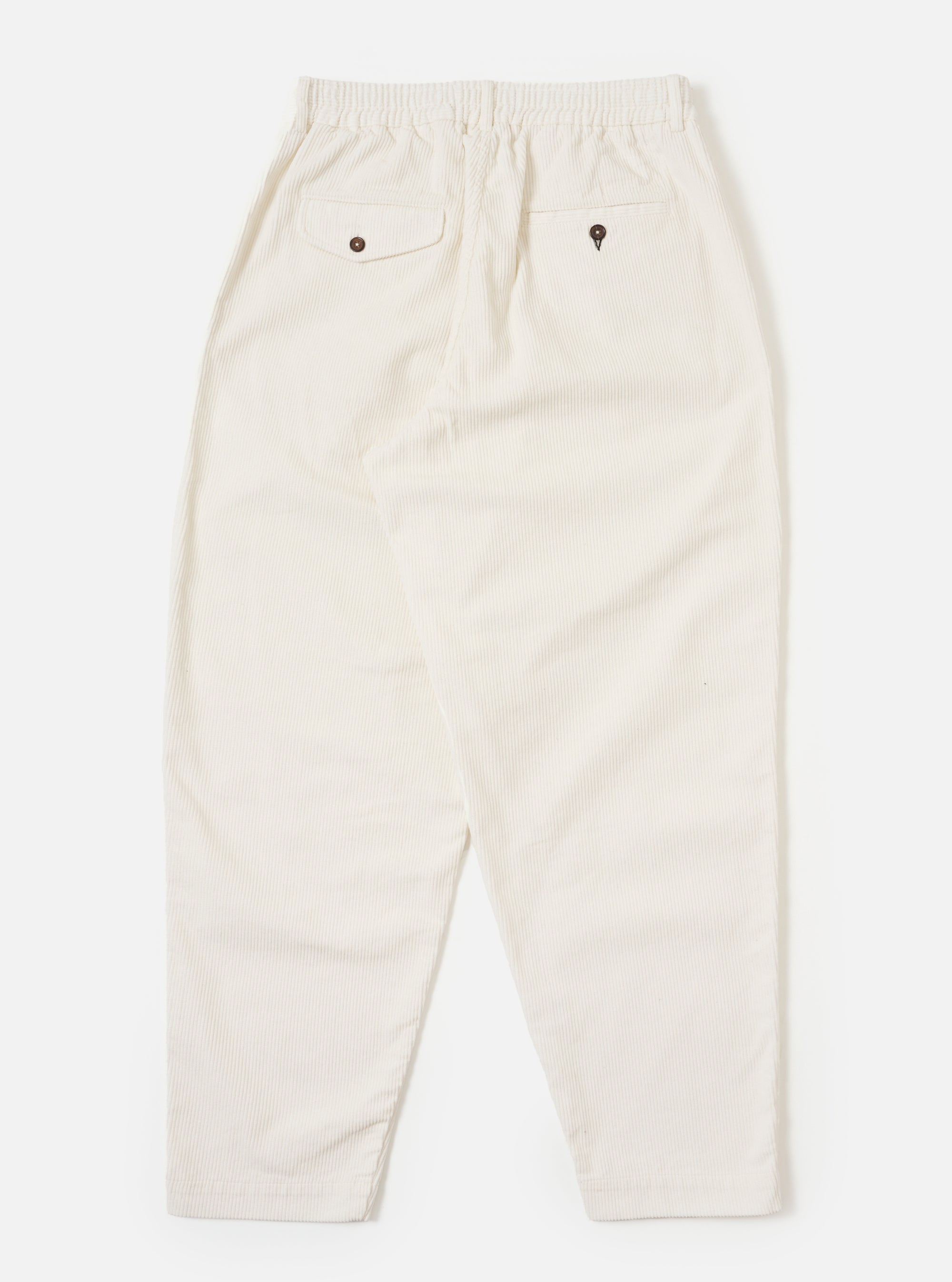 The back of ecru cord pleated track pant on a white background. The corduroy material is visible, as are the two back pockets with button closures.