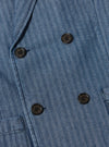 Close-up of the Indigo Denim Herringbone Manor Jacket, showcasing the blue herringbone pattern, dark buttons, and tailored fit. The image highlights the jacket's texture and design details.
