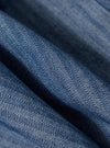 Close-up of the Indigo Denim Herringbone Manor Jacket, showcasing the blue herringbone pattern and denim texture. The fabric is draped to highlight its quality.