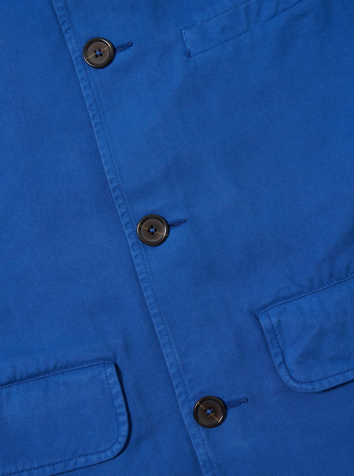 Close-up of the navy Derek Twill Warmus Jacket, showcasing the twill texture, buttons, and pocket detail. The jacket is neatly laid out on a flat surface.