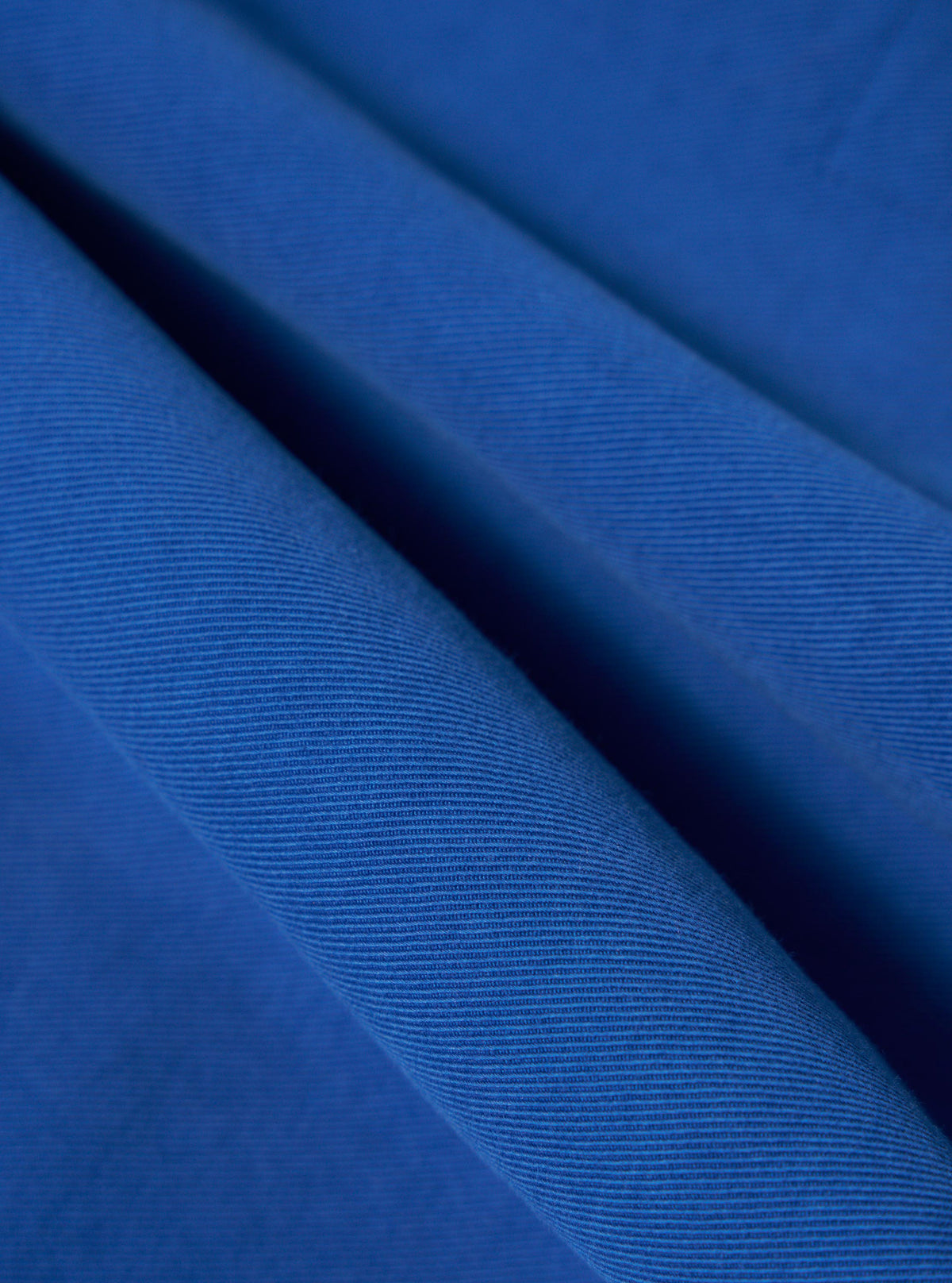 Close-up of the navy Derek Twill Warmus Jacket fabric. The twill weave is visible in the bright blue material, which is draped to show texture.