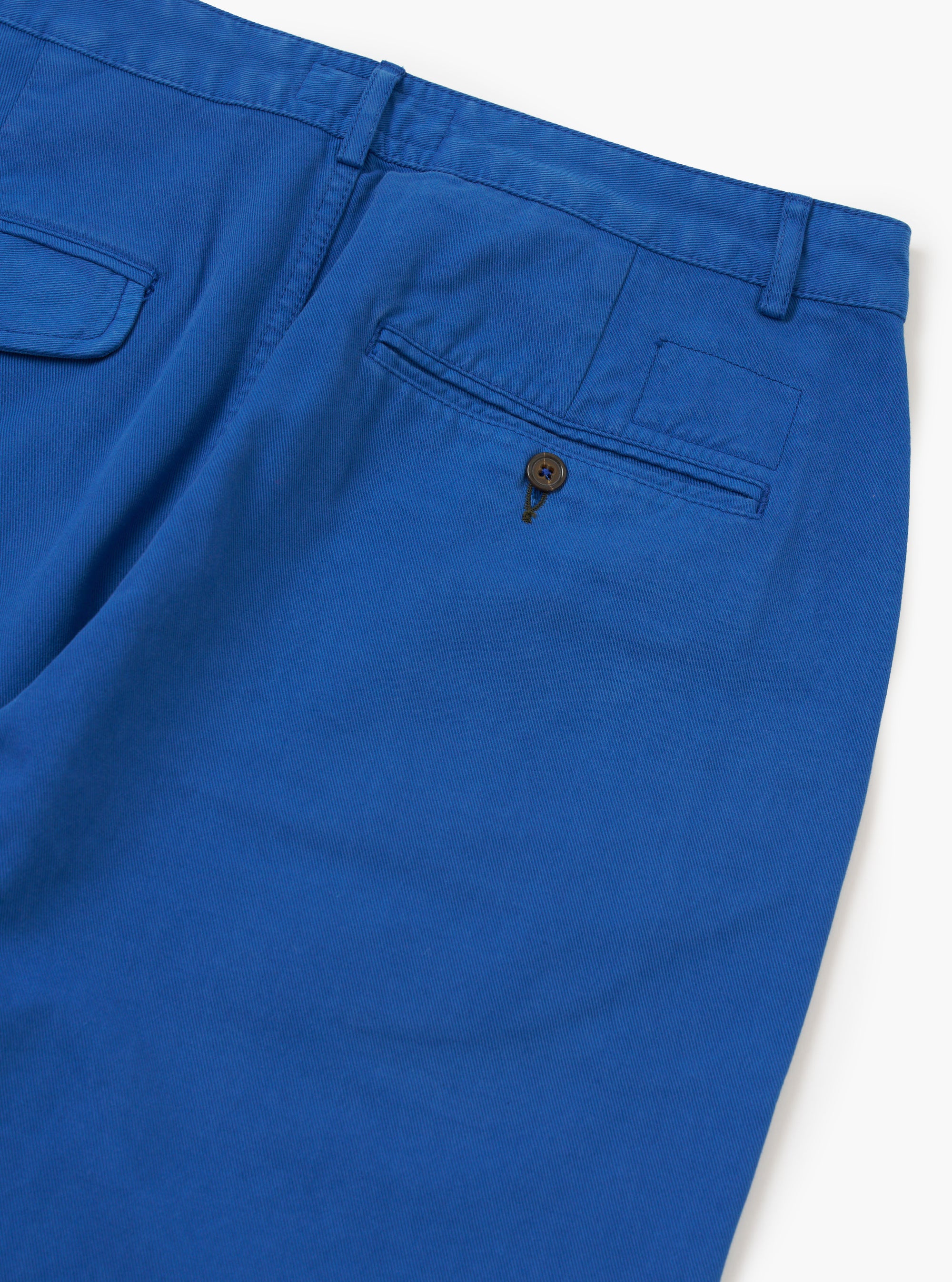 Close-up of the back of Navy Derek Twill Super Chino pants on a white surface. The twill texture and back pocket with button closure are visible.