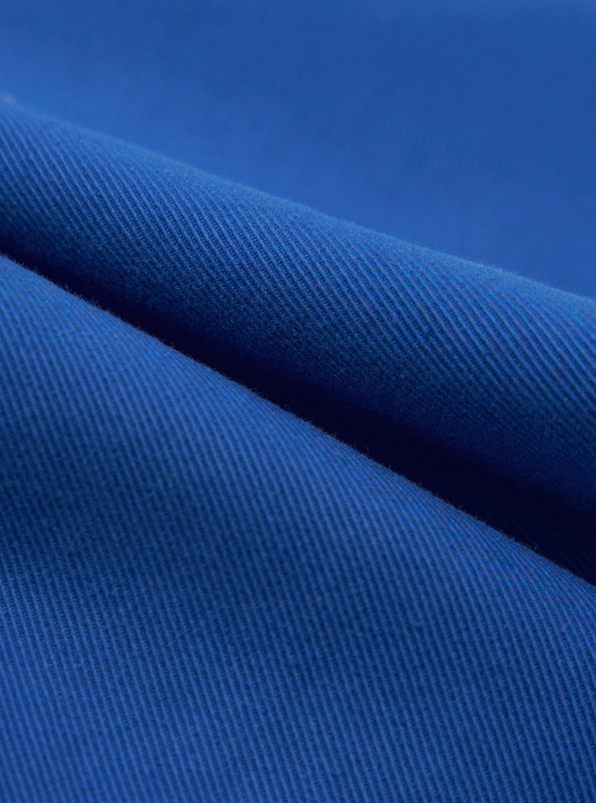 Close-up of the Navy Derek Twill Super Chino fabric. The twill weave is visible, showing the texture and color of the material. The fabric is draped on a plain surface.