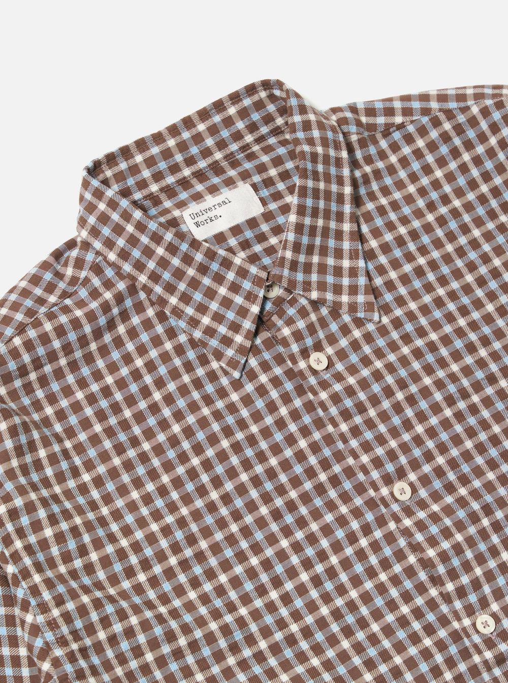 Close-up of the Brown Madison Check Station Shirt on a white background. The shirt has a brown, white, and blue check pattern and white buttons.