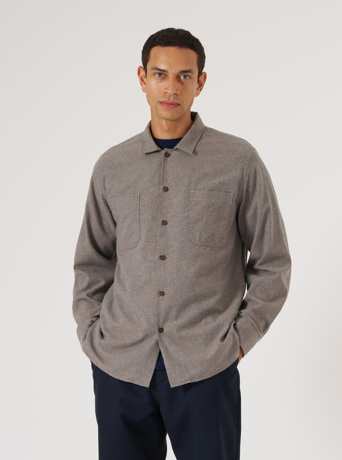 A man models a brown brushed flannel work shirt against a white backdrop. The shirt has two chest pockets and brown buttons.
