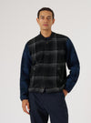 A man models the Grey Moh Check Fleece Button Front Bomber. The bomber has a grey and black check pattern on the front and blue sleeves. The background is a plain white.