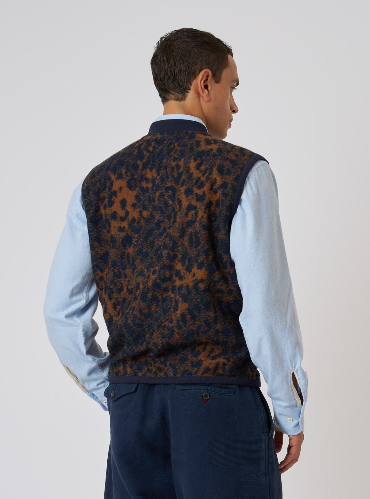 A man in a Dark Navy/Brown Night Leopard Zip Waistcoat, styled with a light blue shirt and dark trousers, stands against a plain white background.