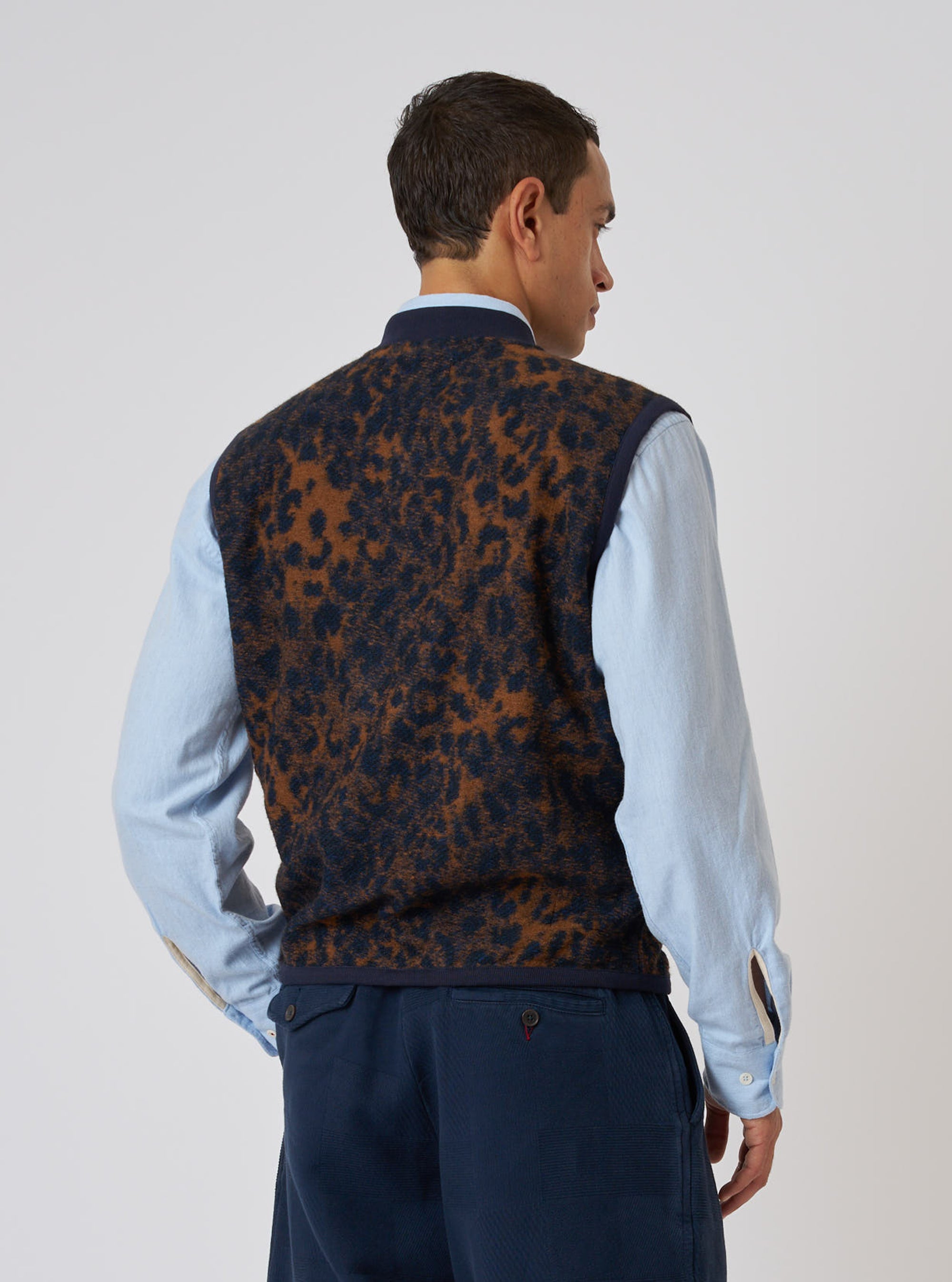 A man in a Dark Navy/Brown Night Leopard Zip Waistcoat, styled with a light blue shirt and dark trousers, stands against a plain white background.