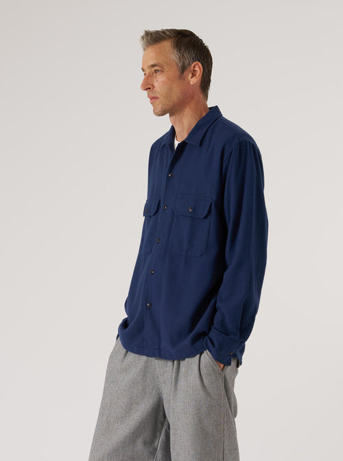 A man poses in a Navy Alaska Cotton Utility Shirt. The shirt is a relaxed fit, made of cotton. He also wears grey pants. Shot in a studio with a white background.