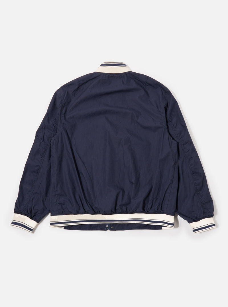 The Navy Peached Poplin NS Bomber Jacket is shown from the back as a flat lay against a plain white background. The image highlights the jacket's smooth navy blue fabric, a simple one-piece back panel, and tonal ribbed detailing at the collar, cuffs, and hem.