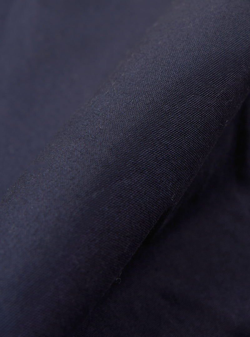 A close-up fabric swatch of the Navy Peached Poplin NS Bomber Jacket highlights the smooth, matte texture and deep navy blue color of the peached poplin material. The fabric fills the frame, providing a detailed view of the garment's weave and finish.