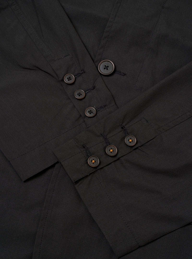 The Black Recycled Polytech Capitol Jacket is shown in a close-up detail shot as a flat lay against a plain white background. The image focuses on the lower front section of the garment, highlighting a large patch pocket with a flap closure and the smooth, technical texture of the black recycled polytech fabric. Clean tonal stitching and a straight hem are visible.