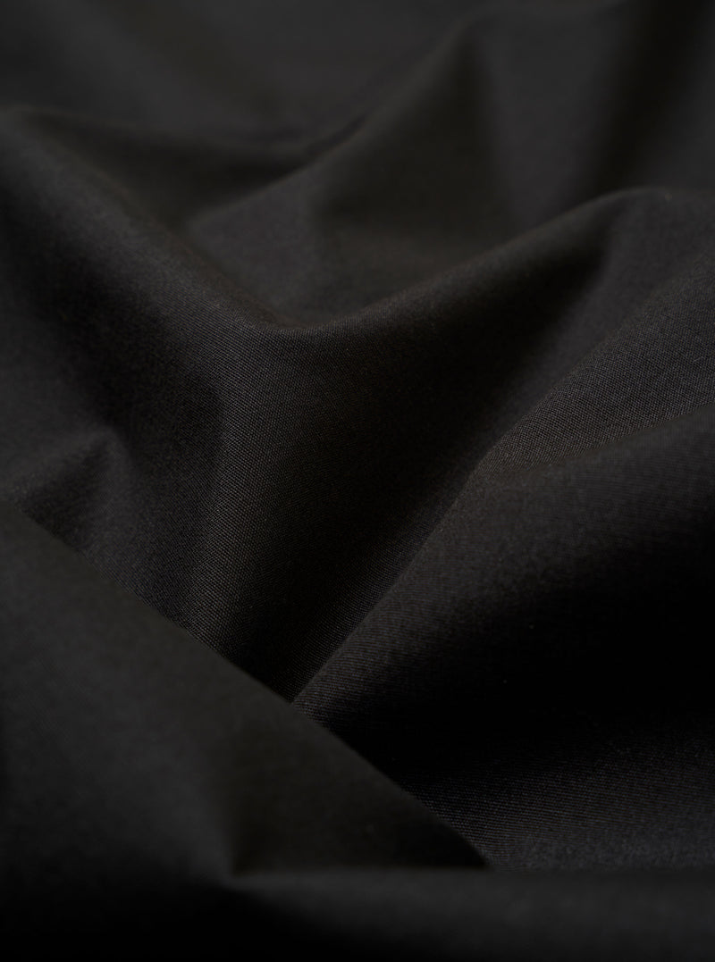 The Black Recycled Polytech Capitol Jacket is shown from a rear three-quarter angle as a flat lay against a plain white background. The image highlights the jacket's unstructured design, featuring a single back vent and a smooth black fabric with a subtle technical sheen.
