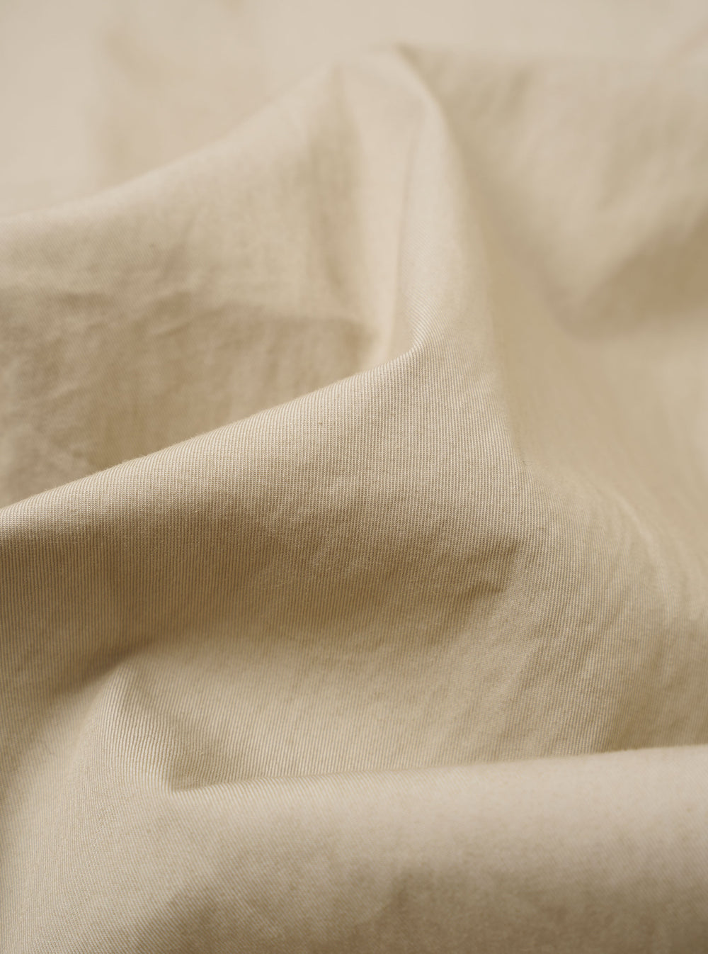 The Sand Cotton Recycled Nylon Mix Daley Jacket is shown in a detail shot as a flat lay against a white background. The image focuses on the upper portion of the garment, highlighting the drawstring hood, the top of the two-way central zipper, and the smooth texture of the sand-colored fabric.