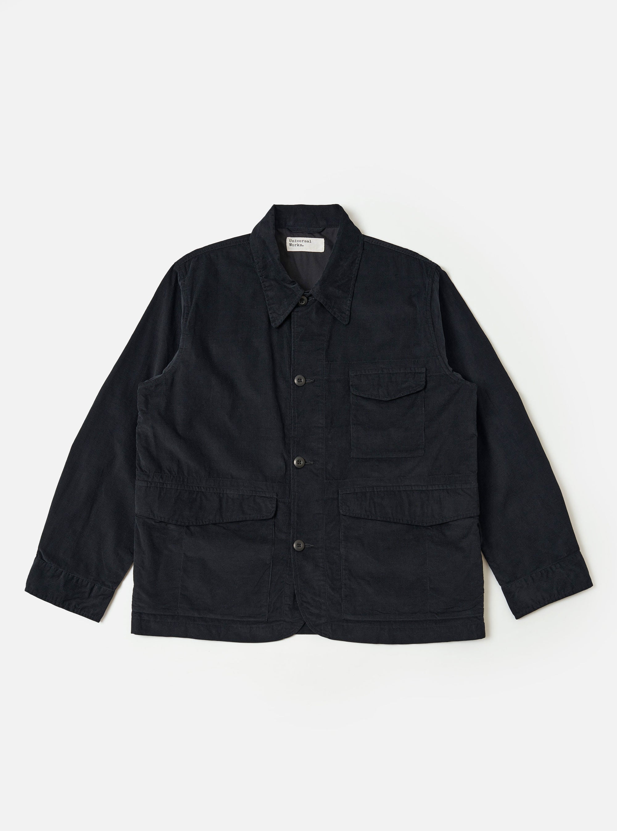 The Black Organic Fine Cord Duty Jacket is shown as a flat lay against a plain white background. The jacket features a spread collar, a central button-front closure, two large double-flap hip pockets, and a single chest patch pocket. The fine-wale corduroy texture is visible across the black organic cotton fabric.
