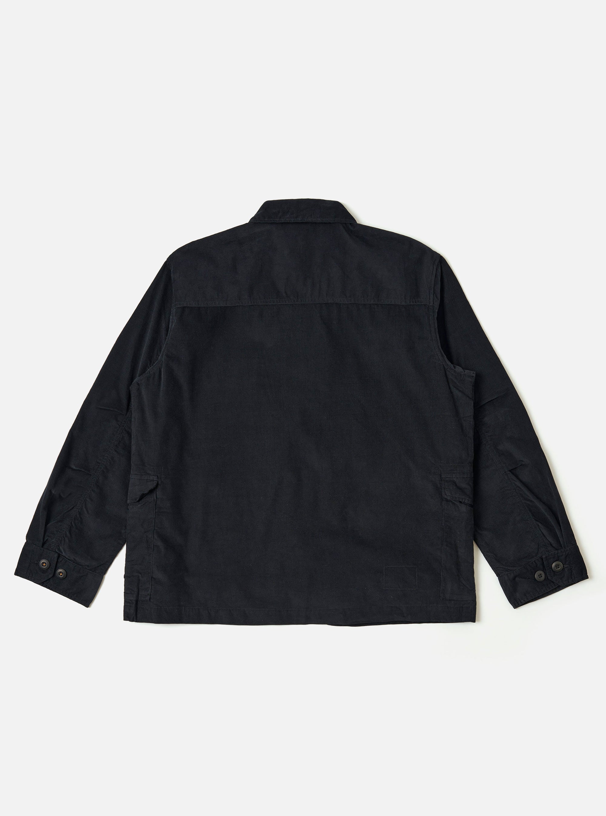 The Black Organic Fine Cord Duty Jacket is shown from the back as a flat lay against a plain white background. The image highlights the jacket's oversized fit, loose sleeves with darting at the elbows, and a curved rear hem. The fine-wale organic cotton corduroy texture is visible throughout the garment.