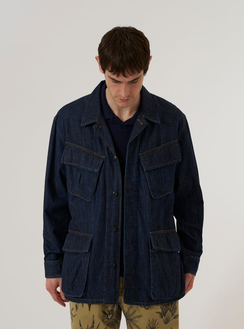 A model wears the Indigo Kaihara LT WT Denim Jungle Jacket over a light-colored top, standing against a plain white background. The jacket is crafted from deep indigo denim and features four large front patch pockets with button closures and a full-length buttoned front.