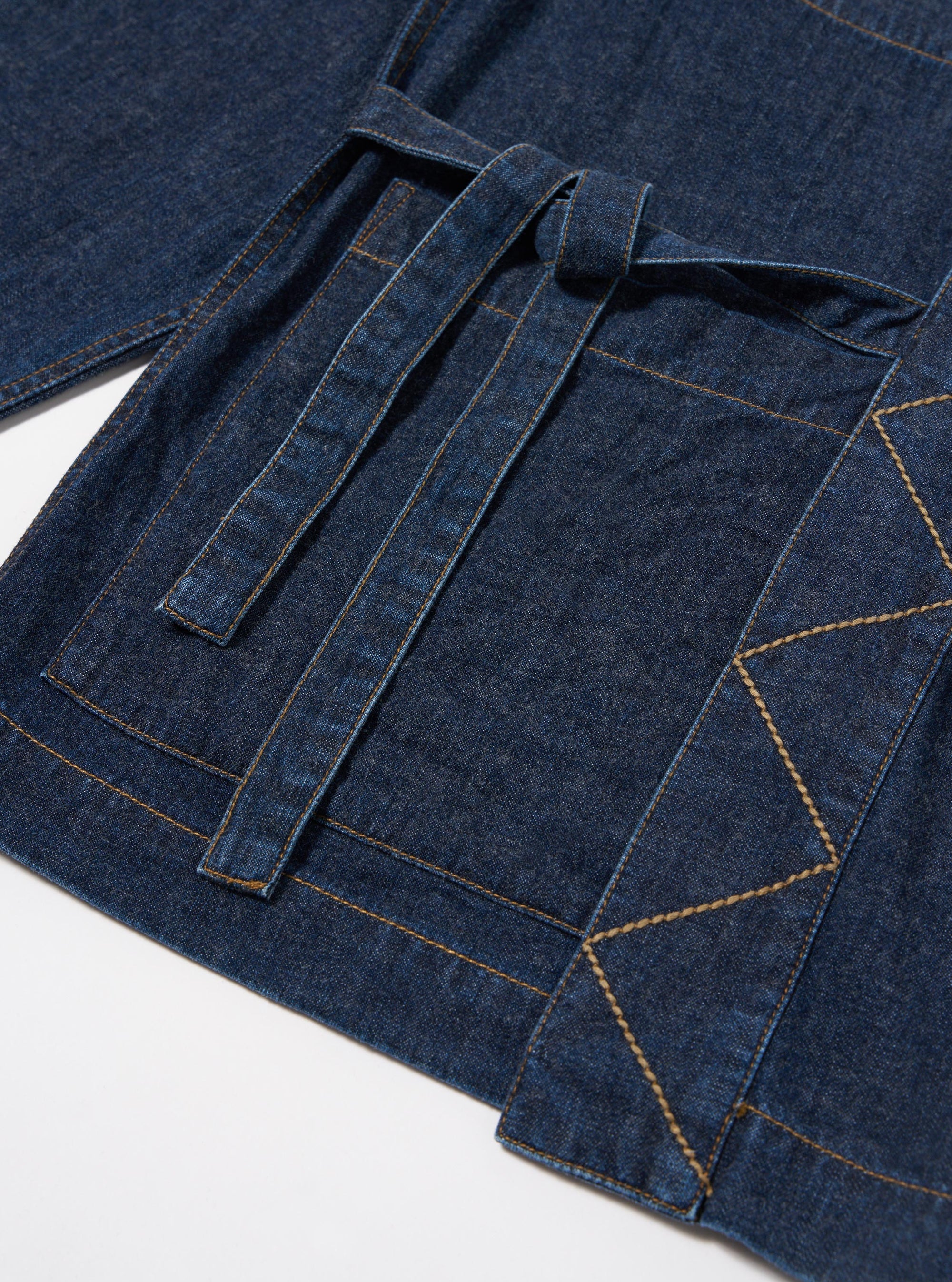 The Indigo Kaihara LT WT Denim Kyoto Work Jacket is shown from the back as a flat lay against a plain white background. The image highlights the clean construction of the garment, featuring a simple straight hem and the wrap-around fabric ties visible at the sides.