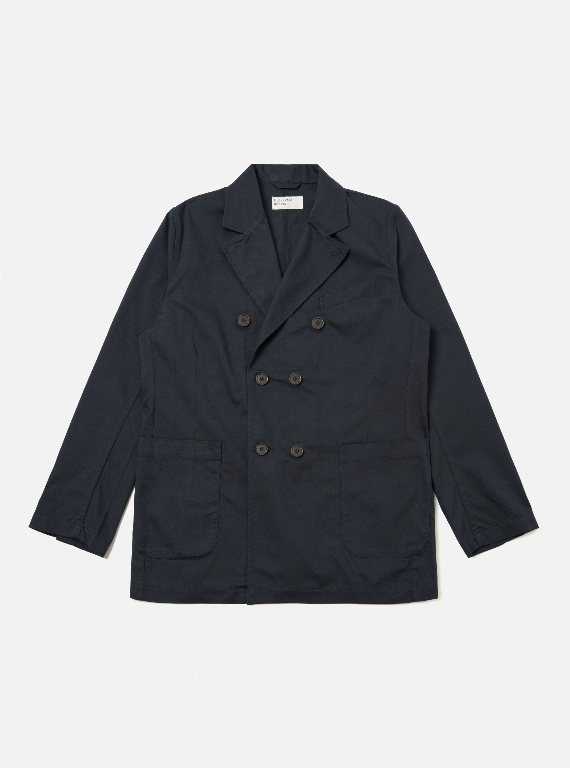 The Navy Twill Manor Jacket is presented as a flat lay against a plain white background. The jacket features a double-breasted front with six buttons, three of which are used for closure. It has two lower patch pockets, a welt chest pocket, and a notched lapel. The navy blue cotton twill fabric has a visible diagonal weave.