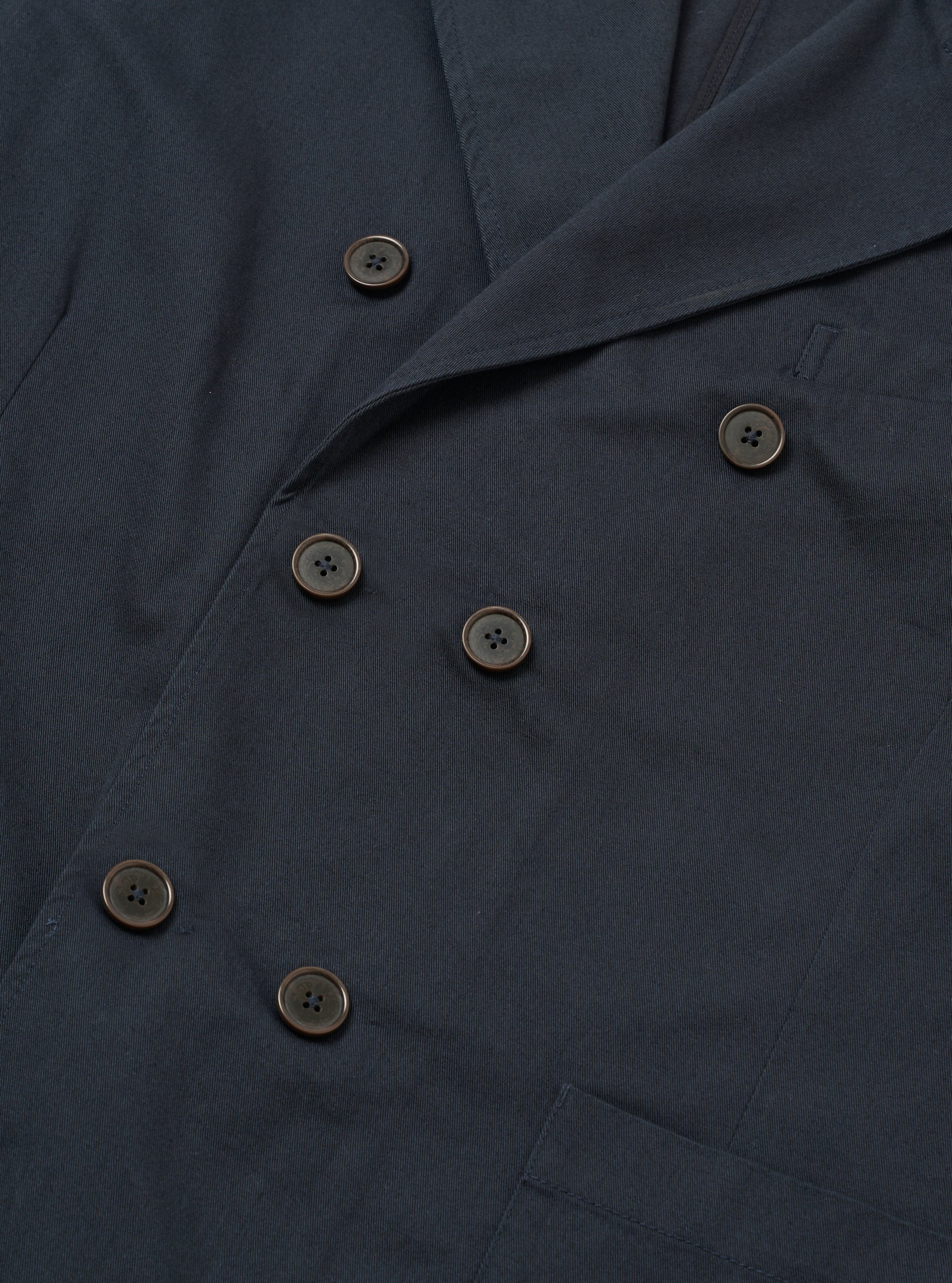 The Navy Twill Manor Jacket is shown from the back as a flat lay against a plain white background. The image highlights the double vents at the hem, the structured shoulders, and the smooth navy blue cotton twill fabric.