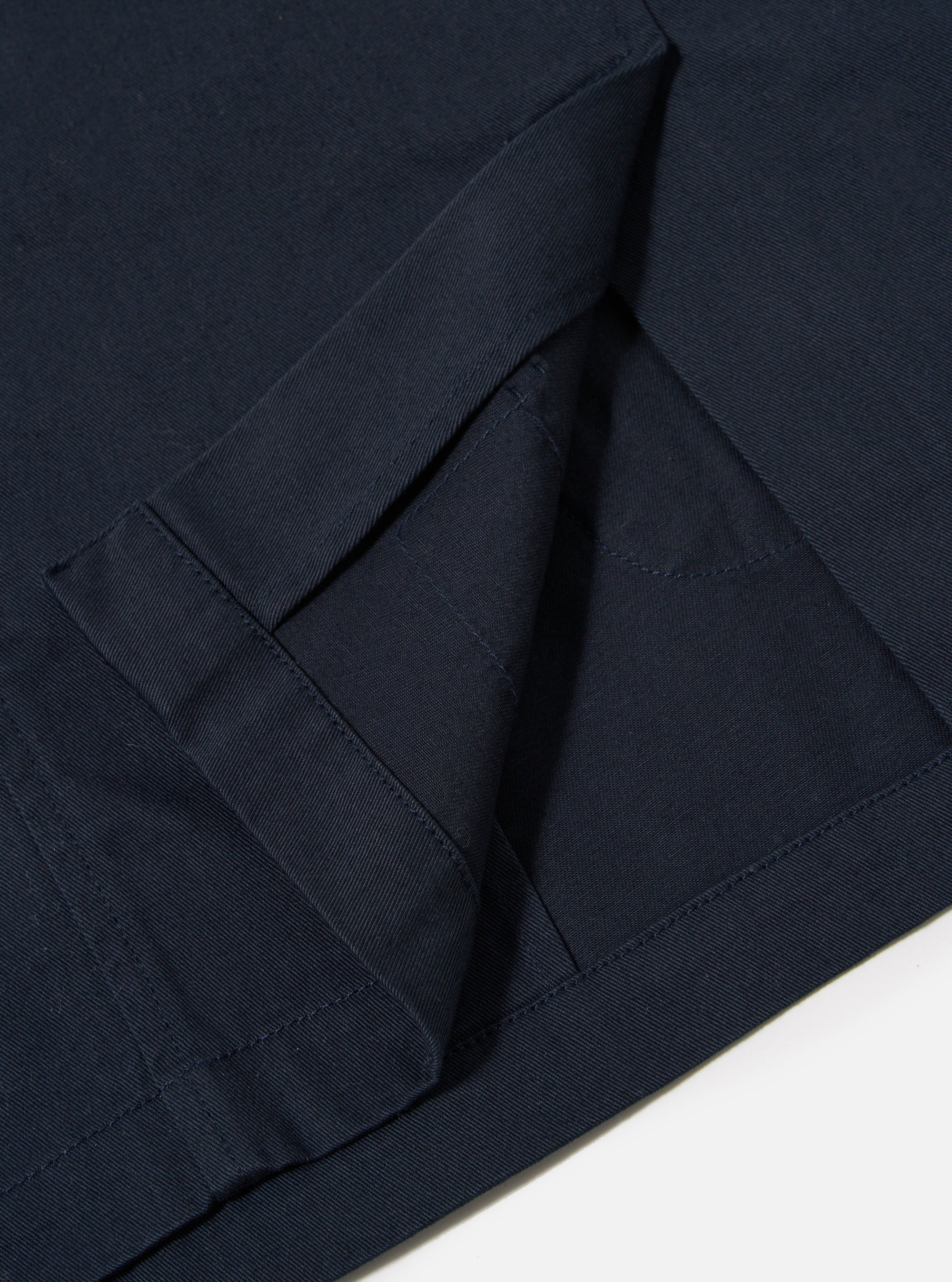 The Navy Twill Manor Jacket is displayed as a flat lay against a plain white background. The jacket is a double-breasted style with a four-button front and features two large patch pockets at the hips and a single welt pocket on the chest. The navy blue cotton twill fabric has a visible diagonal weave.