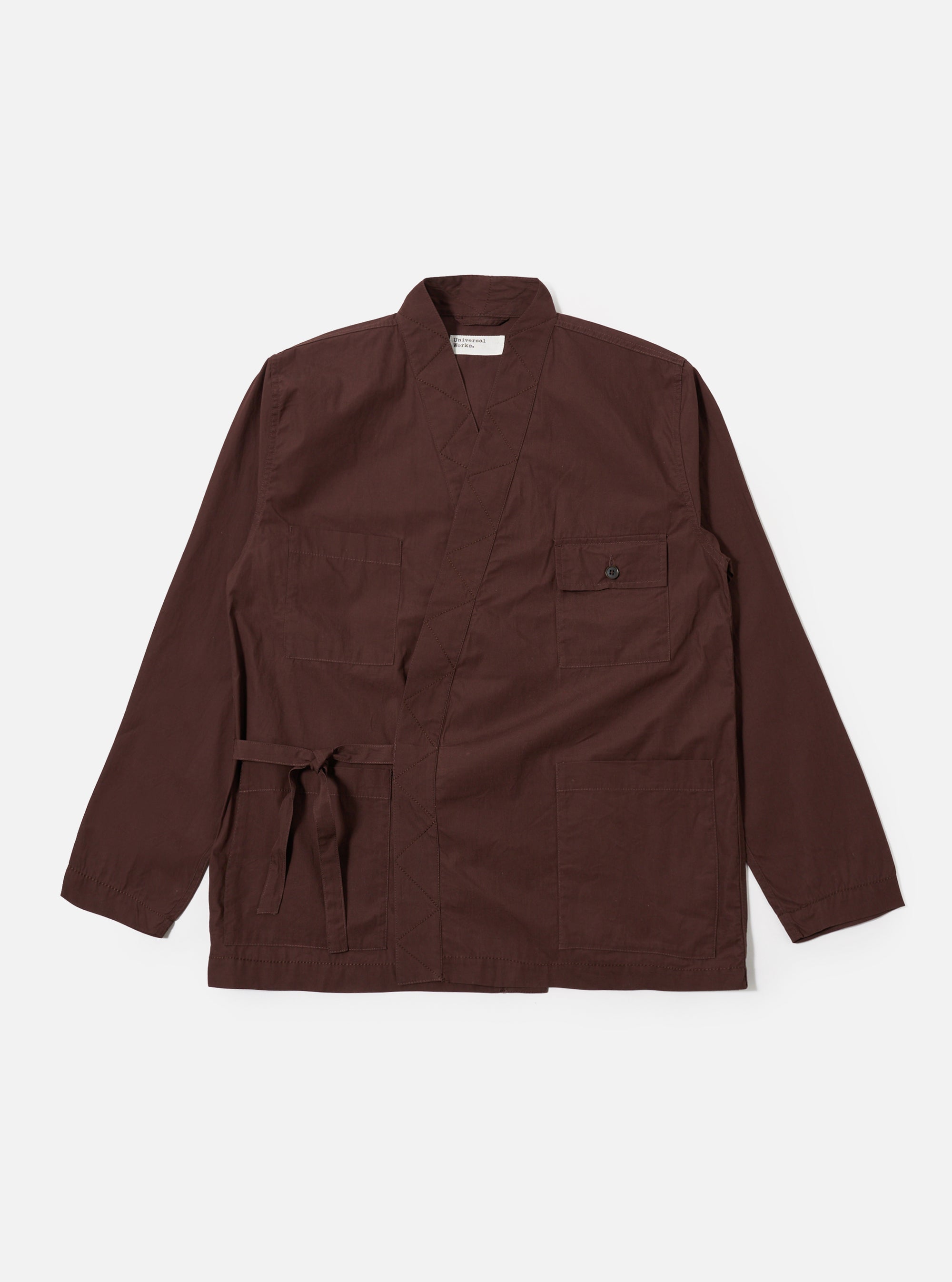 The Brown Peached Poplin Osaka Work Jacket is shown as a flat lay against a white background. The jacket features a wrap-front design with external ties, two lower patch pockets, and two chest patch pockets, one of which has a button-down flap. The brown cotton fabric has a smooth, matte finish.