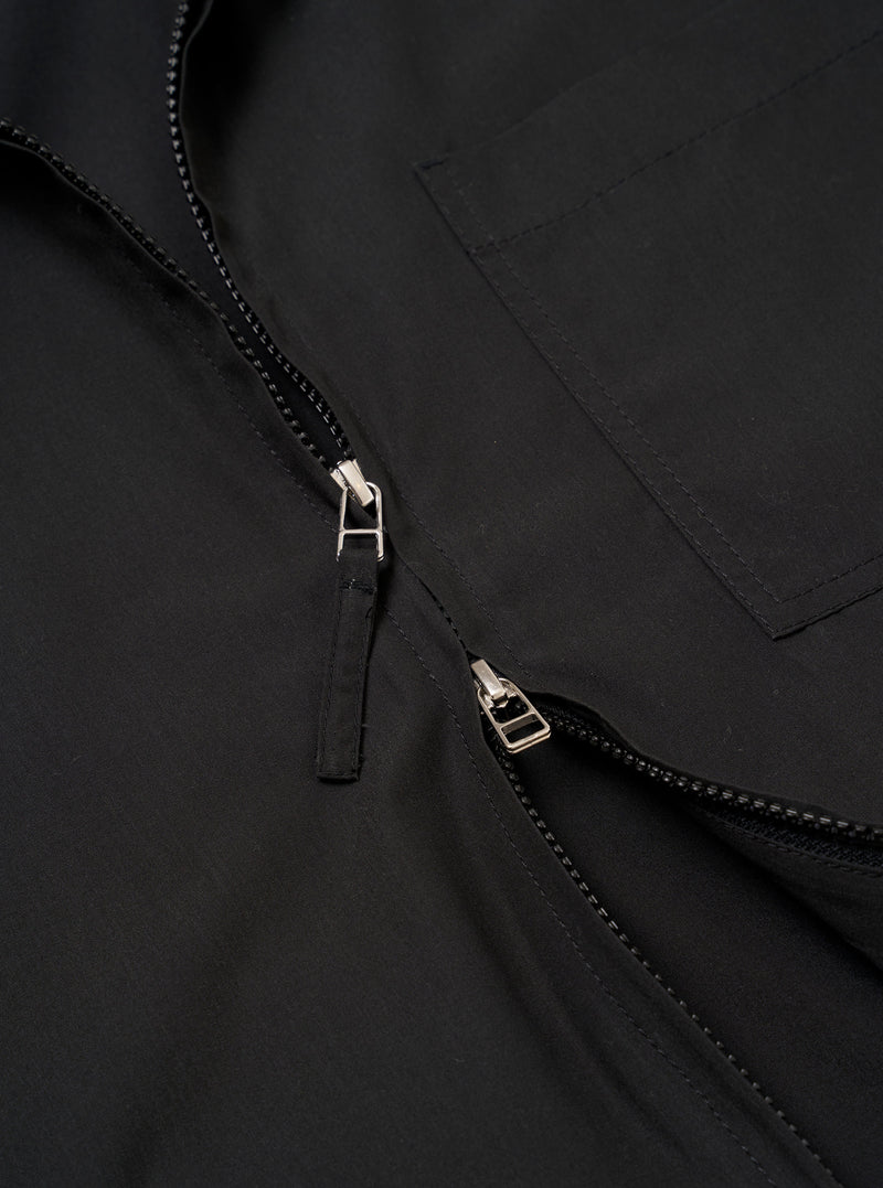 The Black Recycled Polytech Rose Bowl Jacket is shown in a close-up detail shot as a flat lay against a plain white background. The image highlights the technical texture of the black fabric and the construction of the front pockets and the central two-way zipper closure.