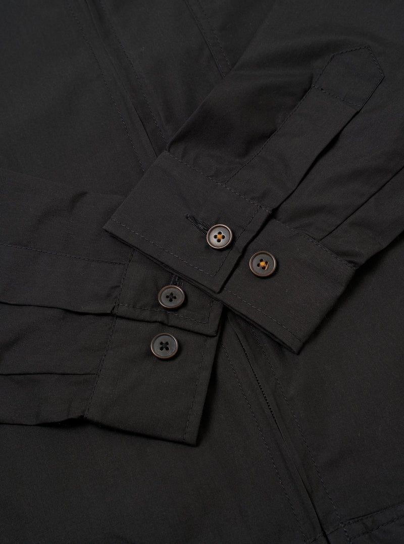 The Black Recycled Polytech Rose Bowl Jacket is shown from the back as a flat lay against a plain white background. The image highlights the jacket's simple construction, featuring a straight hem with adjustable button tabs on either side and vertical pleats extending from the shoulder yoke to the hem.