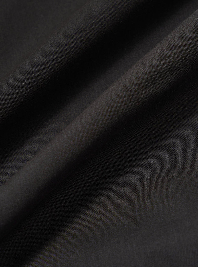A close-up swatch image of the Black Recycled Polytech Rose Bowl Jacket highlights the smooth, technical texture of the black recycled polytech fabric. The material fills the frame, providing a detailed view of the garment's color and construction.
