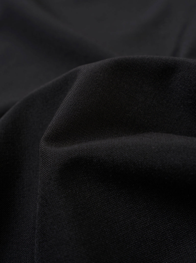 The Black Tropical Suiting Two Button Jacket is shown as a flat lay against a plain white background. The jacket features a classic two-button front closure, notched lapels, and two large patch pockets at the hip. The fabric appears smooth with a subtle sheen, characteristic of tropical suiting.