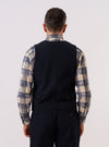 A model wears the Dark Navy Ospina Cotton Field Waistcoat over a light-colored shirt, shown from a rear three-quarter angle against a plain, neutral studio background. The waistcoat features a structured back with vertical seams and a straight hem. The dark navy fabric has a subtle seersucker texture.