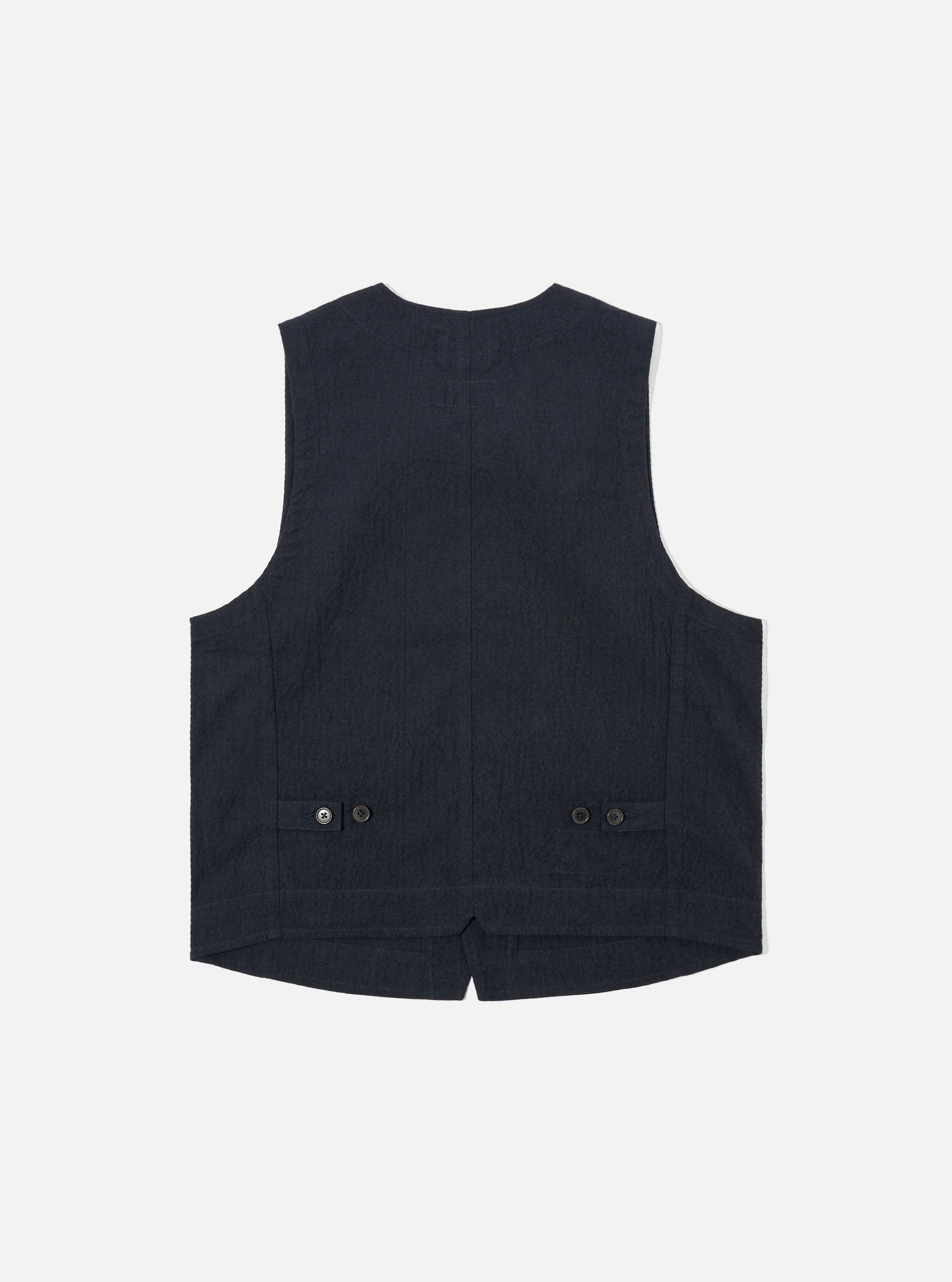 The Dark Navy Ospina Cotton Field Waistcoat is displayed as a flat lay from a side angle against a plain white background. The image highlights the side profile and the armhole of the garment, showcasing the multi-pocket design and the textured dark navy seersucker fabric.