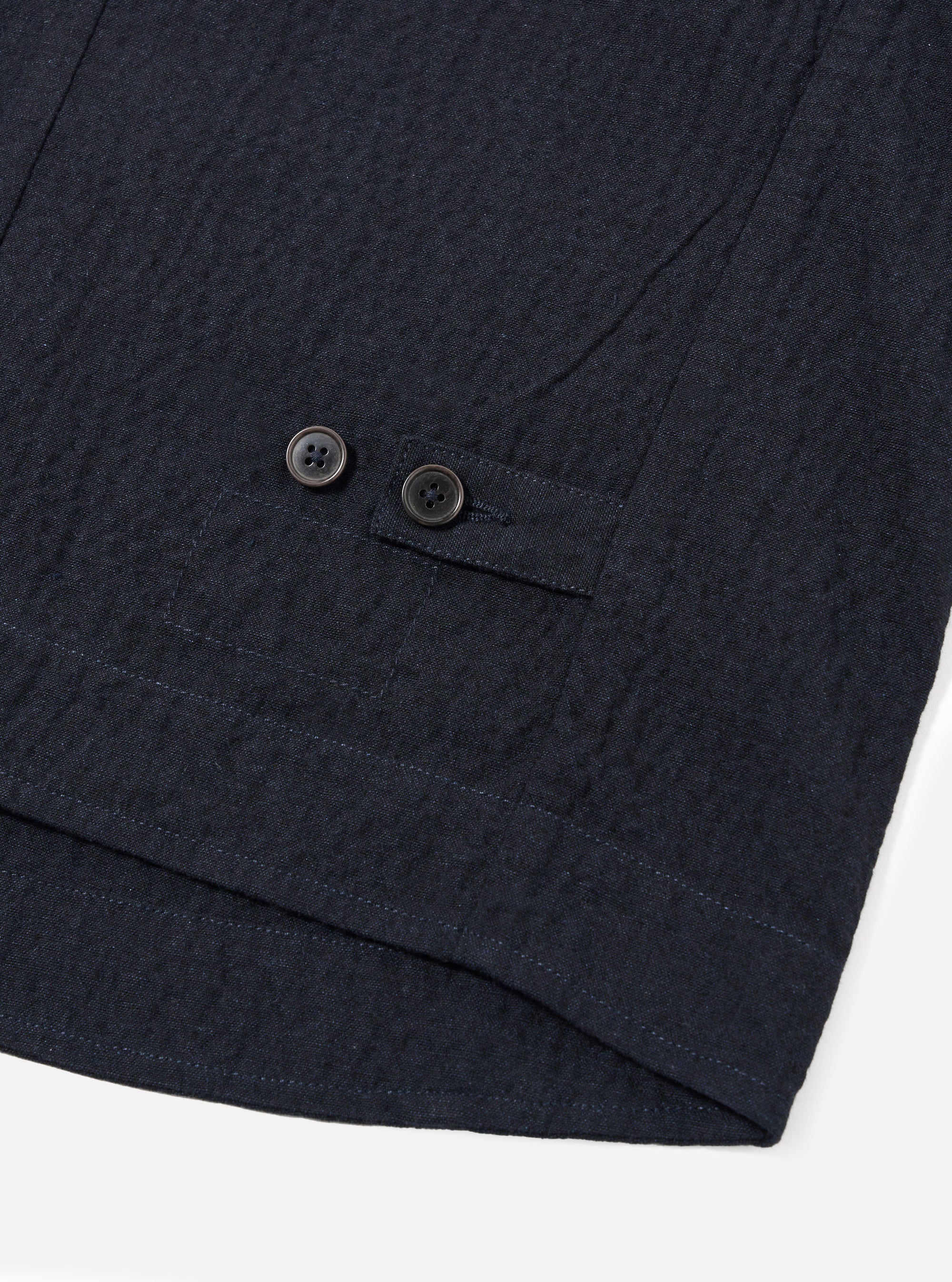 The Dark Navy Ospina Cotton Field Waistcoat is shown in a detail view as a flat lay against a plain white background. The image highlights the textured seersucker finish of the dark navy fabric and the construction of the functional patch pockets.